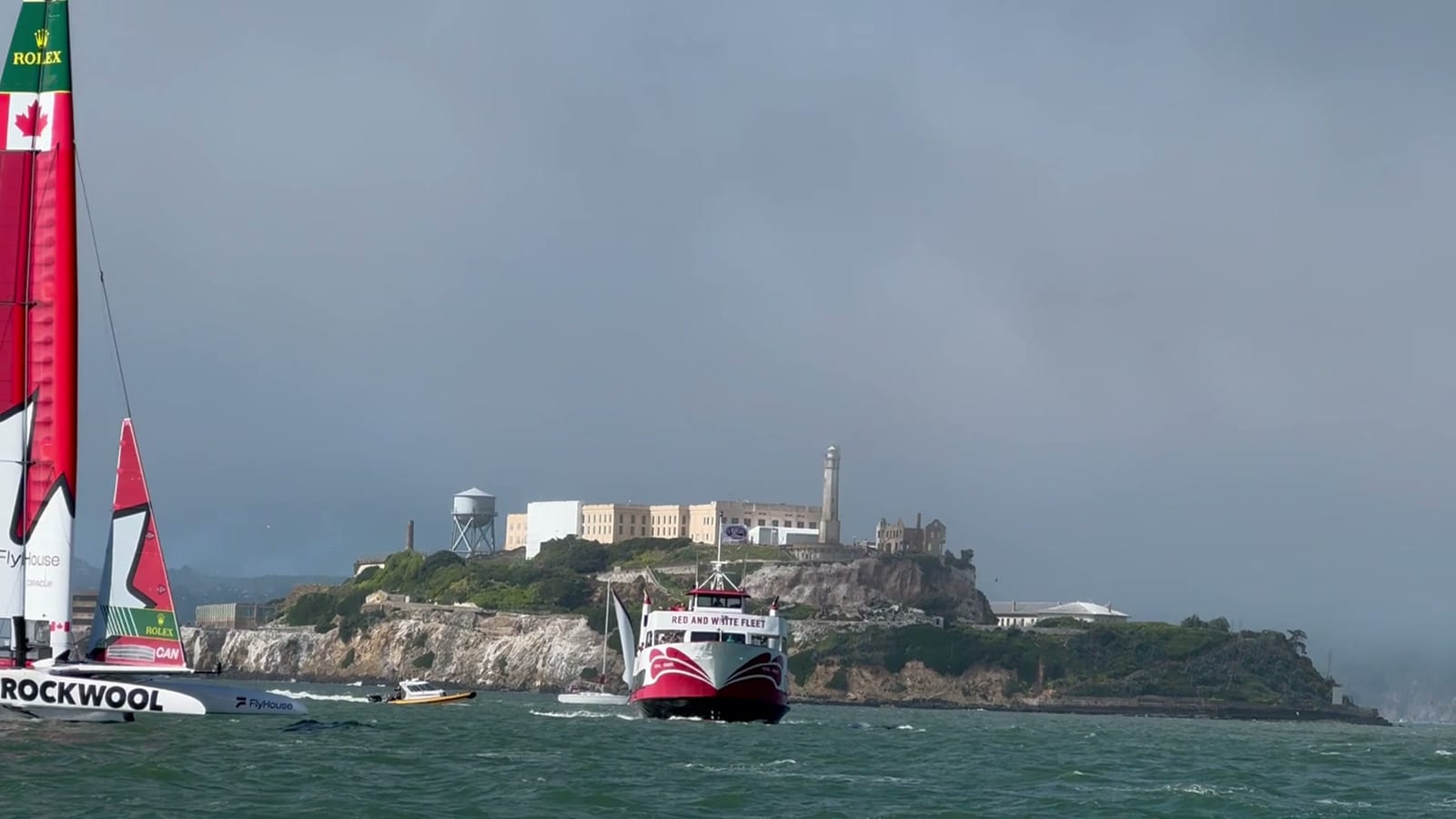 The Canadian SailGP F50 racing past Alcatraz Island with its red and white wing sail, its hull lifted clear of the water